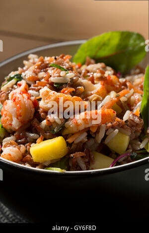 Eine schwarze Schale mit Krebse & Mango Salat mit Reis, Krebse, Mango, Roter Mangold und Rucola mit Chili und Kokos Dressing. Stockfoto