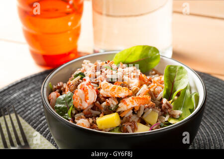 Eine schwarze Schale mit Krebse & Mango Salat mit Reis, Krebse, Mango, Roter Mangold und Rucola mit Chili und Kokos Dressing. Stockfoto