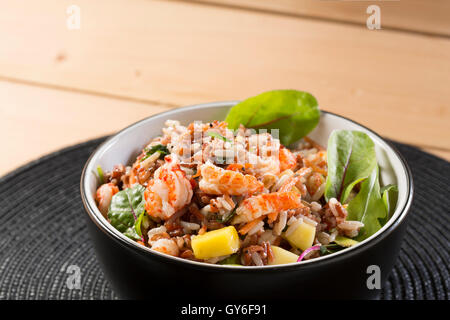 Eine schwarze Schale mit Krebse & Mango Salat mit Reis, Krebse, Mango, Roter Mangold und Rucola mit Chili und Kokos Dressing. Stockfoto