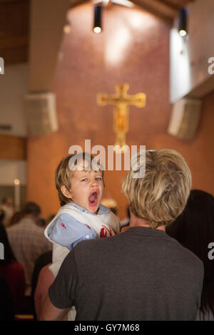 Ein vier Jahre alter Junge gähnt mit Langeweile auf seines Vaters Schulter während der Messe in einer Laguna Niguel, CA, katholische Kirche. Beachten Sie Kreuz im Hintergrund. Stockfoto