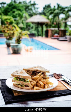 Club Sandwich Snack mit Pommes Frites auf Teller mit Schwimmbad Stockfoto