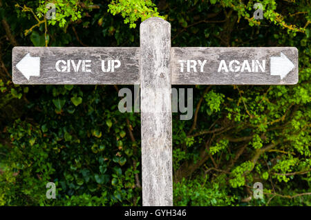 Wegweiser aus Holz mit zwei entgegengesetzte Pfeile über grüne Blätter Hintergrund. GIVE UP versus TRY AGAIN Hinweisschilder Stockfoto