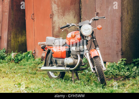 Alte rote Motorrad geparkt auf den grünen Rasen Garten. Generische Oldtimer Motorrad Motorrad In der Landschaft auf Rusty Hintergrund Stockfoto