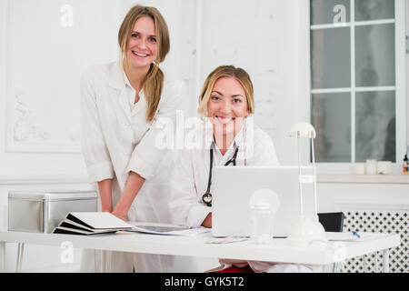 Zwei weibliche freundlich fröhlich Ärzte oder Krankenschwestern isoliert im Büro lächelnd und Blick in die Kamera Stockfoto