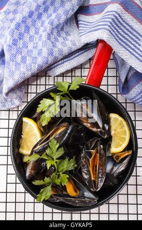 Gekochte Muscheln mit Zitrone und Petersilie in einen roten und schwarzen Emaille-Topf auf Rack-Kühlung Stockfoto