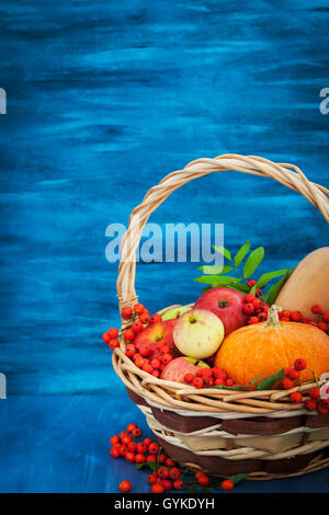 Herbstliche Stillleben mit Kürbisse, Äpfel und Duftspiel in einem Korb auf blauem Hintergrund aus Holz Stockfoto