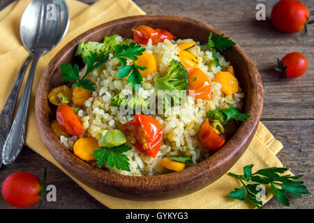 Köstliche hausgemachte vegetarische Bulgur mit Gemüse: Tomaten, Karotten, Zucchini, Brokkoli und Petersilie in rustikalen Holzschale - Stockfoto