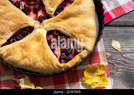 Hausgemachte Kirsche und Apfelkuchen über rustikalen hölzernen Hintergrund mit gelben Blättern, Nahaufnahme - köstliche Herbst Gebäck Stockfoto