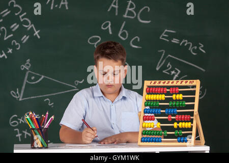 Kleiner Junge beschrieben an die grüne Tafel an Schule denken über die Aufgabe Stockfoto