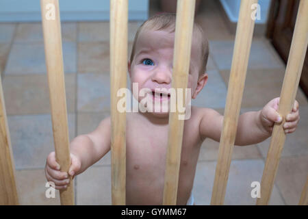 Einjährigen jungen hinter hölzernen Schutzgitter Treppe. Er versucht, nach oben gehen Stockfoto