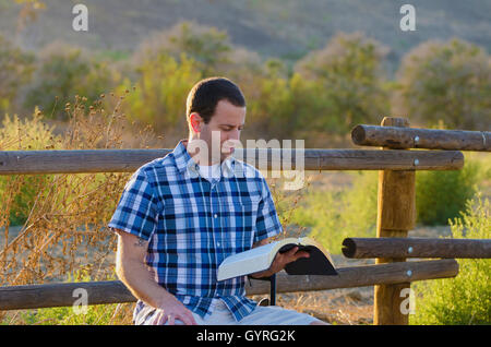 Das Lesen der Bibel im Freien bei Sonnenlicht Pinsel im Hintergrund. Stockfoto