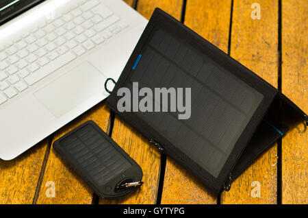 Tragbare solar-Ladegeräte, sitzen auf Holzoberfläche neben Laptops, wie gesehen von oben, moderne Technologie-Konzept Stockfoto