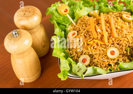 Closeup klassische Präsentation Salat, Reis und Oliven in künstlerischen weißen Teller wie gesehen von oben mit abstrakten Hintergrund, Salz, Pfeffer am Tisch Stockfoto