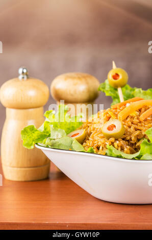 Closeup klassische Präsentation Salat, Reis und Oliven in künstlerischen weiße Teller mit abstrakten Hintergrund Salz Pfefferstreuer auf Tisch Stockfoto