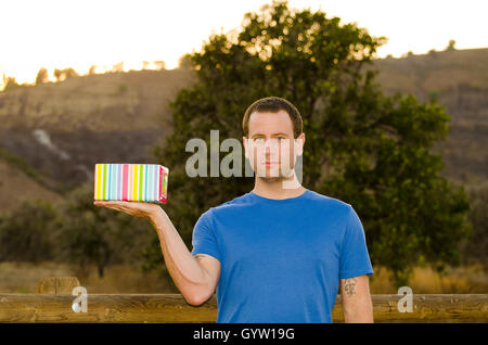 Geschenkgeben? Mann mit schweren Ausdruck hält ein buntes eingewickelt in seine Hand, auf der Seite vorhanden. Stockfoto