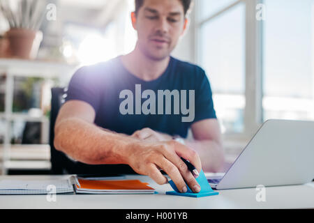 Aufnahme des jungen Mann am Tisch sitzen und reißen einen klebrigen Pfosten aus dem Block. Geschäftsmann, arbeiten an seinem Schreibtisch. Stockfoto