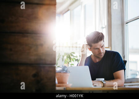 Junger Geschäftsmann mit Problemen und Stress im Büro. Mann an seinem Schreibtisch mit Laptop und schaut Weg zu denken. Stockfoto