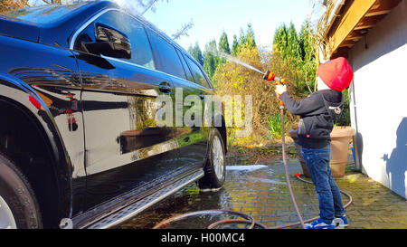 Little boy Duschen ein Auto mit einem Wasserschlauch, Seitenansicht, Deutschland Stockfoto