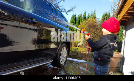 Little boy Duschen ein Auto mit einem Wasserschlauch, Seitenansicht, Deutschland Stockfoto