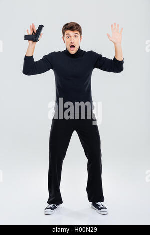 Gesamte Länge der Angst junger Mann hält Gewehr und Aufstehen mit Händen Stockfoto