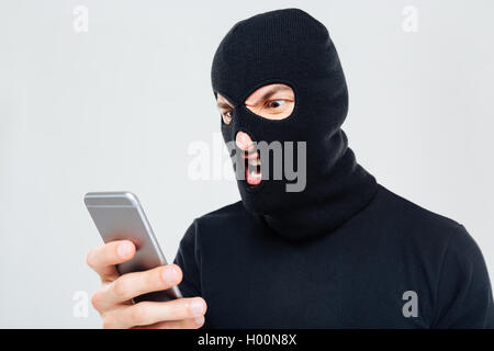 Aggressive junge verrückter in Balaclava stehend und mit Handy Stockfoto