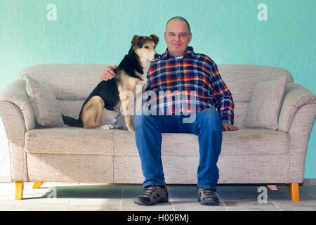 Gemischte Rasse Hund (Canis lupus f. familiaris), Podenco - gemischte Rasse Hund zusammen sitzen im Wohnzimmer mit seinem Master, auf dem Sofa, Deutschland Stockfoto