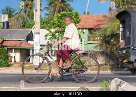 HIKKADUWA, SRI LANKA - 24. Februar 2014: älterer Mann im Sarong und Hemd mit dem Fahrrad. Radfahren ist der Haupttransport f Stockfoto