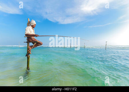 HIKKADUWA, SRI LANKA - 9. März 2014: ältere Stelzenläufer Fischer am Strand von Hikkaduwa. Die meisten realen Stelzenfischer schon lange vorbei. Stockfoto