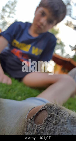 Junge sitzt auf dem Rasen und auf seine schmutzige Socke voller Löcher Stockfoto