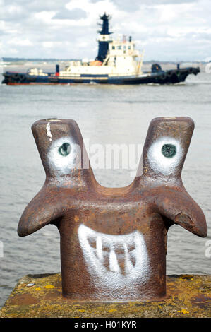 Lustiges Gesicht Spray auf marine Liegeplatz Poller auf dem Fluss Mersey in Liverpool mit Schlepper vorbei im Hintergrund gemalt Stockfoto