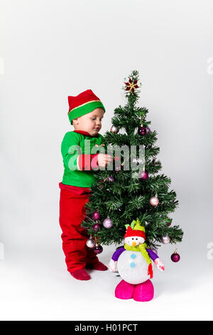 Baby Boy gekleidet wie santa's Helper schmücken Weihnachtsbaum, hängende Ornamente. weißen Hintergrund. Stockfoto