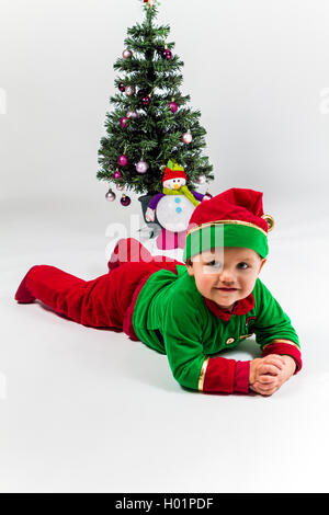 Baby Boy als Santas Helper liegen neben Weihnachtsbaum verkleidet. Weißen Hintergrund. Stockfoto