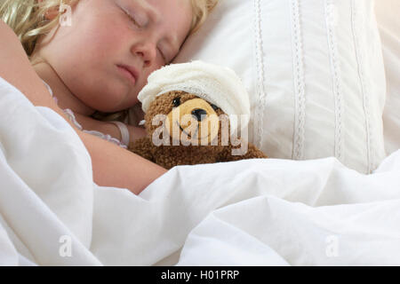 Ein junges Mädchen, schlecht im Bett kuscheln den Teddy, fühlt sich auch schlecht. Stockfoto