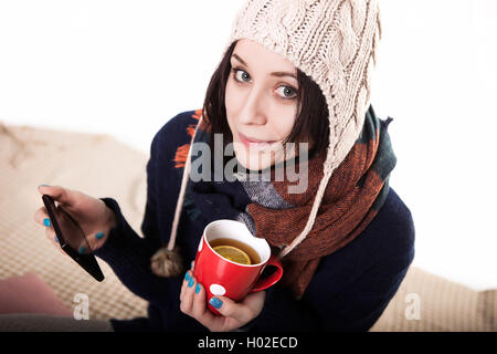 Frau mit Tablet auf gemütliche Atmosphäre zu Hause auf dem Bett. Junge Frau mit Tasse Tee oder Kaffee in Händen, die freie Zeit mit Komfort genießen. Weiches Licht und bequemen Lifestyle-Konzept. Technologie im Leben. Stockfoto