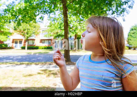 Niedliche blonde kleine Mädchen bläst einen Löwenzahn Stockfoto