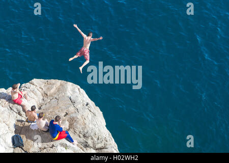 Junger Mann springt von einer Klippe ins Meer. Stockfoto