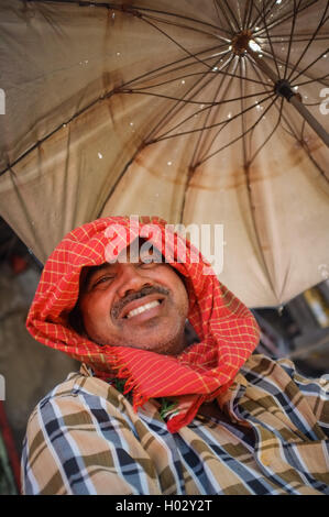 MUMBAI, Indien - 10. Januar 2015: Mann sitzt unter einem Sonnenschirm Stockfoto