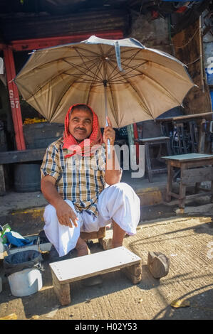 MUMBAI, Indien - 10. Januar 2015: indische Arbeiter sitzen unter einem Sonnenschirm auf Bürgersteig Stockfoto