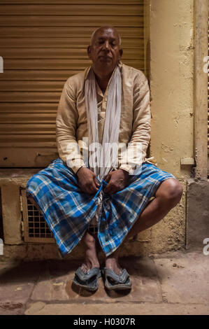 VARANASI, Indien - 20. Februar 2015: indischer Mann sitzen neben geschlossen Shop in Hemd, Schal, Lungi und Hausschuhe. Stockfoto