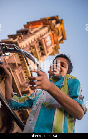 JODHPUR, Indien - 11. Februar 2015: Junge mit dem Fahrrad unter Ghanta Ghar auch bekannt als Uhrturm am Sardar Markt mit Verkehr. Stockfoto