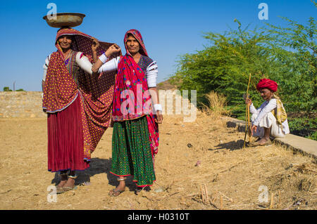 GODWAR REGION, Indien - 14. Februar 2015: Rabari Frauen stehen im Feld tragen Sarees und Oberarm Armbänder mit Mann sitzt in Stockfoto