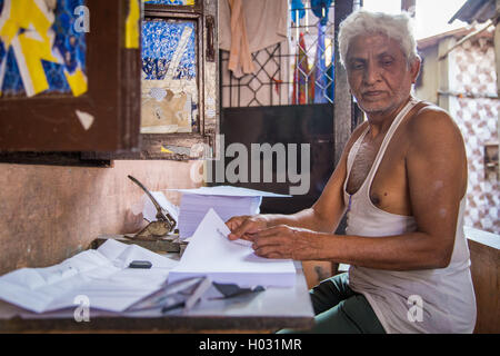 MUMBAI, Indien - 16. Januar 2015: ältere indische Mann sitzt im Freien vor Haus und stanzt Löcher in Wirtschaftszeitung. Stockfoto