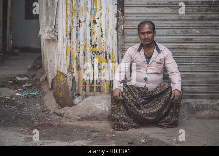 MUMBAI, Indien - 12. Januar 2015: indischer Mann mit Schnurrbart sitzt neben geschlossenen laden in schmutzige leere Straße in Lungi und rosa Shir Stockfoto