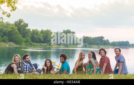 8 junge gut aussehende Erwachsene Verlegung auf dem Rasen in der Nähe von See in sommerlich fühlen Stockfoto