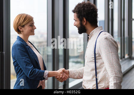 Jungunternehmer und Geschäftsfrau Händeschütteln im modernen Büro Halle. Stockfoto