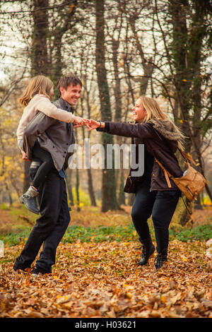 Tochter reitet Vater auf Huckepack mit Mutter neben ihnen im Park an einem Herbsttag. Stockfoto