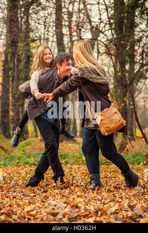 Tochter reitet Vater auf Huckepack mit Mutter neben ihnen im Park an einem Herbsttag. Stockfoto