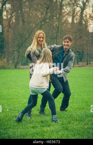 Vater hält Tochter mit Mutter neben ihnen unter Baumkronen. Stockfoto