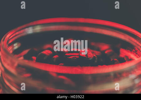 Einmachglas voller Kaffeebohnen, die mit einem roten Leuchten beleuchtet. Rote Bohnen, Kaffeebohnen beleuchtet mit roter LED für eine Retro-Café-Atmosphäre Stockfoto