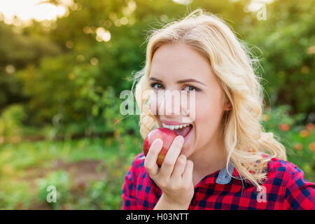 Schöne blonde Frau in Rot kariertes Hemd Essen Apfel Stockfoto